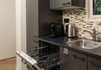 Moderne kitchenette met koffiemachine, waterkoker, gootsteen en open vaatwasser bij Loevestein Lodge in Nederland.