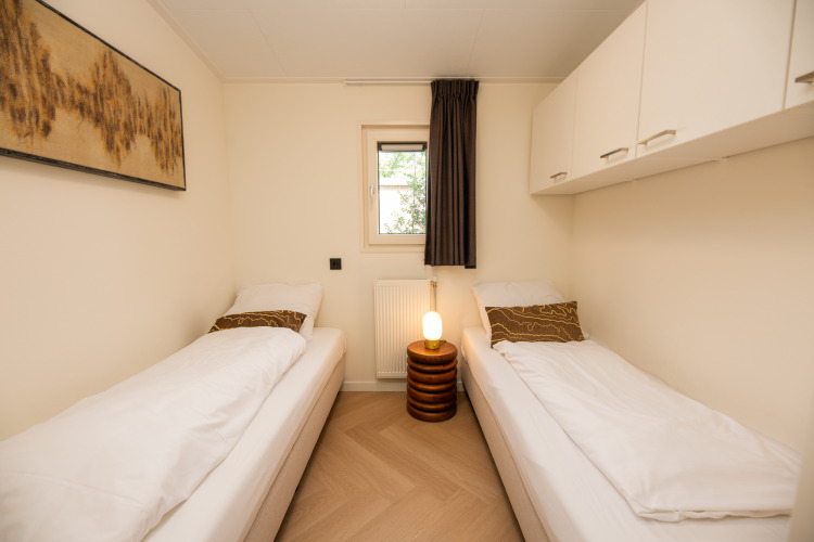 Habitación luminosa con dos camas individuales, armarios blancos y decoración moderna en Veluwepark de Bosgraaf.