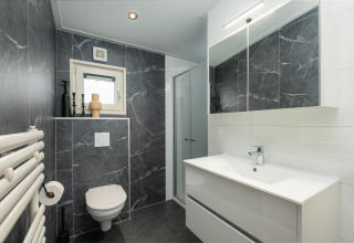 Moderne badeværelse med mørke marmordelen, toilet, bruser, håndvask og stort spejl på Loevestein, Veluwepark de Bosgraaf.