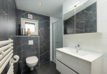 Moderne badeværelse med mørke marmordelen, toilet, bruser, håndvask og stort spejl på Loevestein, Veluwepark de Bosgraaf.