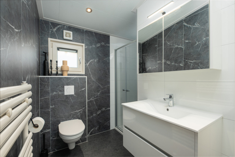 Modernes Badezimmer mit dunklen Marmordetails, WC, Dusche und Waschbecken im Loevestein, Veluwepark de Bosgraaf, Niederlande.