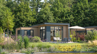 Moderne Lodge in Essenburgh, umgeben von üppigem Garten und Bäumen, mit Terrasse am Seeufer.