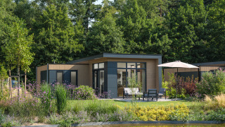 Lodge moderne à Essenburgh entouré de jardin luxuriant et d’arbres, avec terrasse au bord d’un étang.