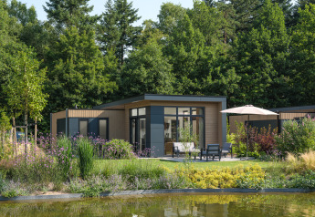 Moderne lodge ved Essenburgh, omgivet af frodig have og træer, med terrasse og siddepladser ved sø.