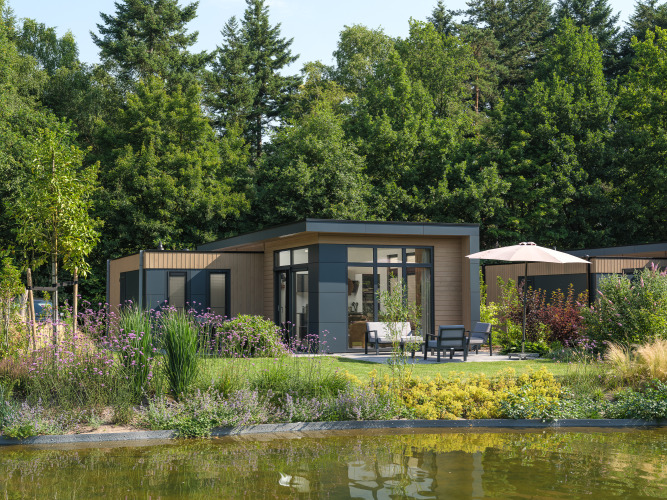 Lodge moderno en Essenburgh rodeado de jardín frondoso y árboles, con terraza junto a un estanque.