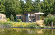 Moderne Lodge mit Glasfront, Terrasse und Sonnenschirm am Wasser im Veluwepark de Bosgraaf, Niederlande.