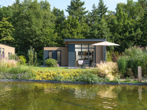 Modern lodge with large windows, terrace and umbrella by a pond at Veluwepark de Bosgraaf, Netherlands.
