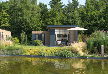 Lodge moderne aux grandes fenêtres, terrasse et parasol au bord d’un étang, Veluwepark de Bosgraaf, Pays-Bas.