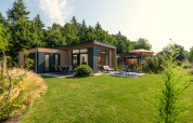 Moderne Lodge in Essenburgh im Veluwepark de Bosgraaf, Niederlande, umgeben von grünem Garten und Wald.