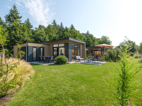Modern lodge at Essenburgh in Veluwepark de Bosgraaf, Netherlands, surrounded by lush garden and trees.