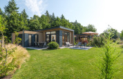 Moderne lodge bij Essenburgh in Veluwepark de Bosgraaf, Nederland, met tuin en veel groen eromheen.