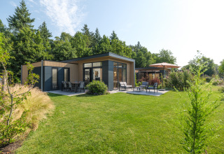 Lodge moderno en Essenburgh, Veluwepark de Bosgraaf, Países Bajos, rodeado de jardín verde y árboles altos.