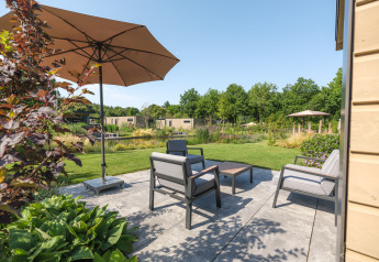 Udendørs terrasse ved lodge Essenburgh i Veluwepark de Bosgraaf, Holland, med havemøbler og parasol.