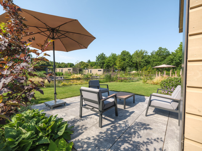 Terraza exterior en la cabaña Essenburgh en Veluwepark de Bosgraaf, Países Bajos, con muebles de jardín y sombrilla.