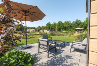 Terraza exterior en la cabaña Essenburgh en Veluwepark de Bosgraaf, Países Bajos, con muebles de jardín y sombrilla.