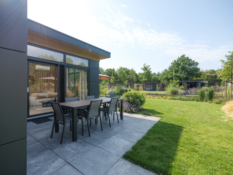 Modern lodge patio with outdoor dining table and lawn at Veluwepark de Bosgraaf, Netherlands.