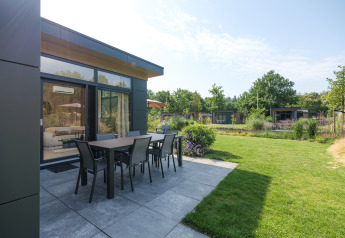 Patio di lodge moderno con tavolo esterno e prato a Veluwepark de Bosgraaf, Paesi Bassi.