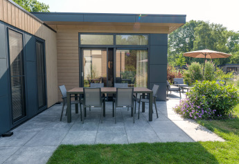 Moderne lodge Essenburgh med terrasse og havemøbler i Veluwepark de Bosgraaf, Holland, omgivet af grønt.