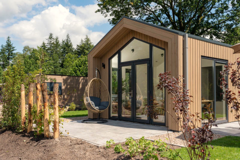 Tiny house moderne avec terrasse, portes vitrées et fauteuil suspendu à Veluwepark de Bosgraaf aux Pays-Bas.