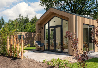 Tiny house moderne avec terrasse, portes vitrées et fauteuil suspendu à Veluwepark de Bosgraaf aux Pays-Bas.