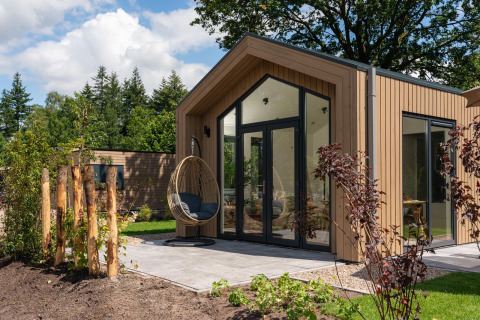 Casa tiny moderna con terraza, paredes de vidrio y silla colgante en Veluwepark de Bosgraaf, Países Bajos.
