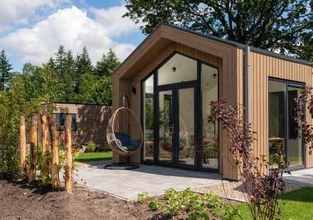 Moderne tiny house met terras, glazen deuren en hangstoel bij Veluwepark de Bosgraaf in Nederland.