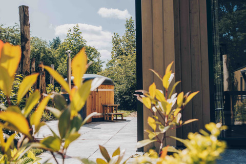 Vista esterna da una tiny house con rivestimento in legno e vasca idromassaggio a Veluwepark de Bosgraaf, Paesi Bassi.