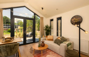 Helles Tiny House Wohnzimmer mit großen Fenstern, Sofa, Esstisch und modernem Dekor mit Gartenblick.