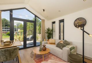 Lichte tiny house woonkamer met grote ramen, een sofa, eettafel en modern decor met zicht op de tuin.