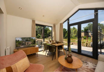 Modernes Tiny House Wohnzimmer mit großen Fenstern, Essbereich, Sofa, Fernseher und Außenausblick.