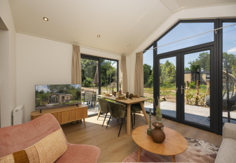 Soggiorno moderno in una tiny house con grandi finestre, tavolo da pranzo, TV e vista sull'esterno verde.