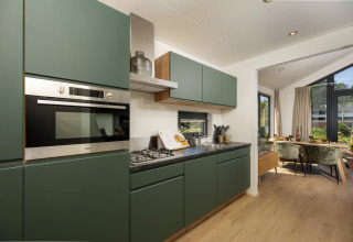 Cuisine moderne de tiny house avec placards verts, coin repas, grandes fenêtres et vue sur le jardin.