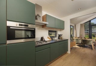 Cocina moderna y compacta en una tiny house, con armarios verdes, zona de comedor y vistas al jardín.
