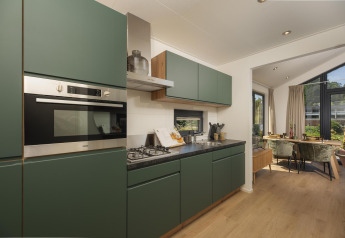 Cocina moderna y compacta en una tiny house, con armarios verdes, zona de comedor y vistas al jardín.