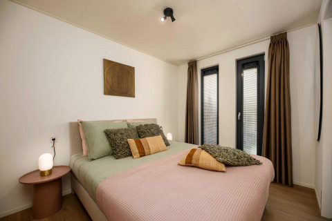 Chambre lumineuse dans une tiny house avec lit double, décoration moderne et grandes fenêtres avec rideaux.