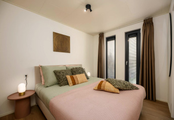 Helles Schlafzimmer in einem Tiny House mit Doppelbett, moderner Einrichtung und großen Fenstern.