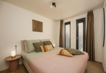 Dormitorio luminoso en una tiny house con cama doble, decoración moderna y grandes ventanas con cortinas.