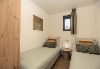 Pequeño dormitorio en una tiny house con dos camas individuales, ventana pequeña y decoración moderna.