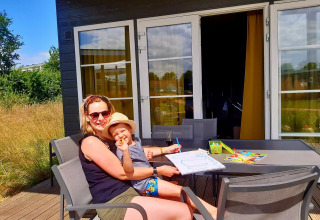 Mama en kind genieten samen van tekenen aan een buitentafel bij een vakantiehuisje in Kompas Camping Nieuwpoort, West-Vlaanderen.