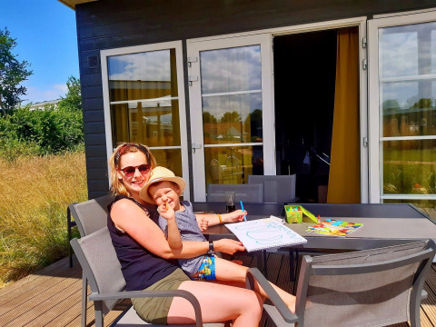 Mama en kind genieten samen van tekenen aan een buitentafel bij een vakantiehuisje in Kompas Camping Nieuwpoort, West-Vlaanderen.