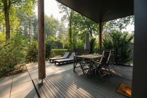 Udendørs terrasse ved Sand Lodge Comfort, Veluwepark de Bosgraaf, med spisebord og liggestole i naturen.