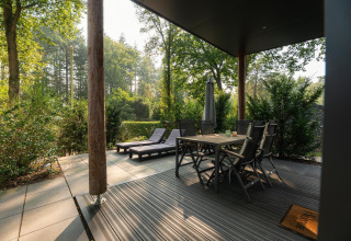 Udendørs terrasse ved Sand Lodge Comfort, Veluwepark de Bosgraaf, med spisebord og liggestole i naturen.