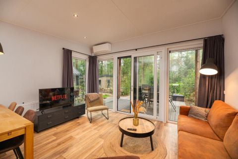 Stue med sofa, TV med Netflix, spisebord og store vinduer i Sand Lodge Comfort, Veluwepark de Bosgraaf.