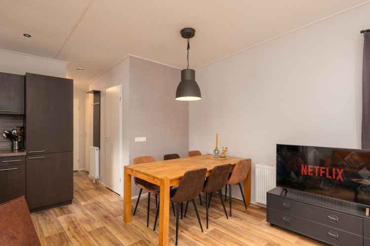 Dining and living area in Sand Lodge Comfort at Veluwepark de Bosgraaf, the Netherlands, with Netflix on TV.