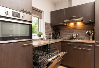 Cocina moderna en Sand Lodge Comfort en Veluwepark de Bosgraaf, Países Bajos, con lavavajillas abierto.
