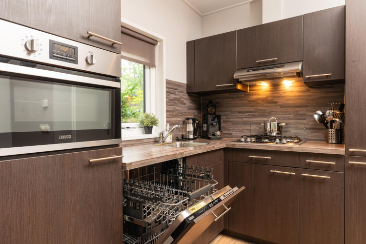 Modern kitchen in Sand Lodge Comfort at Veluwepark de Bosgraaf, Netherlands, with open dishwasher.