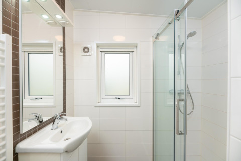 Moderne badeværelse på Sand Lodge Comfort i Veluwepark de Bosgraaf, Holland, med brusebad og håndvask.