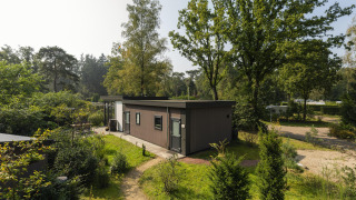 Heather Lodge dal design moderno immerso nel verde, circondato da alberi alti e sentieri nella natura.
