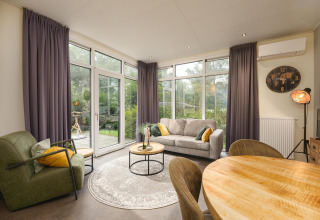 Sala moderna en Heather Lodge de Veluwepark de Bosgraaf, Países Bajos, con grandes ventanales y decoración.