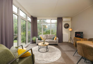 Salón moderno en Heather Lodge en Veluwepark de Bosgraaf, Países Bajos, con grandes ventanales y decoración elegante.